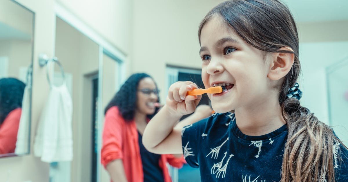 Young girl brushing her teeth in the bathroom with parental supervision, promoting healthy dental habits.
